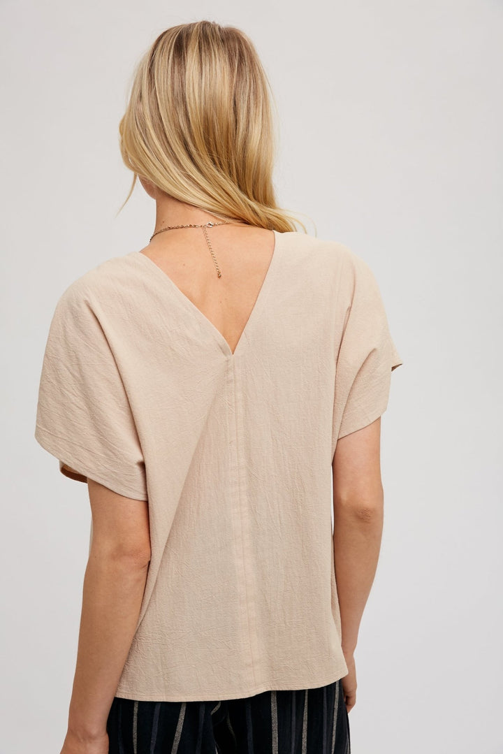 woman wearing a beige FUN2FUN V-neck top with dolman sleeves, showcasing the back v.