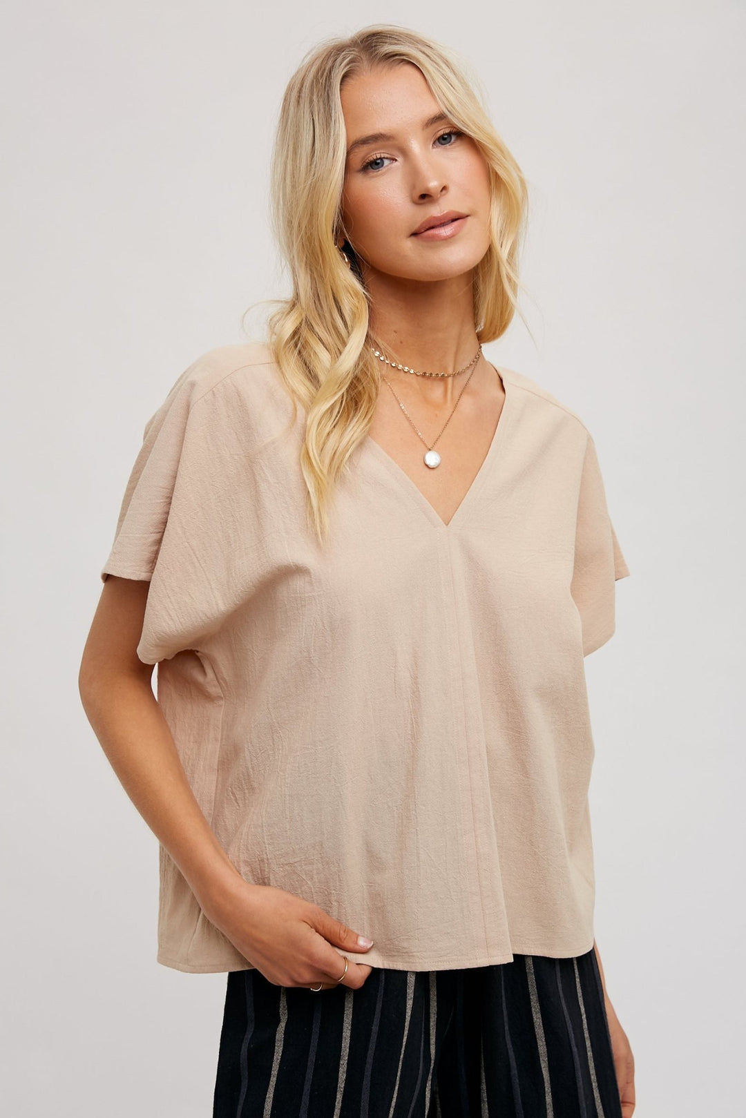 woman wearing a beige FUN2FUN V-neck top with dolman sleeves, showcasing a relaxed and elegant fit.