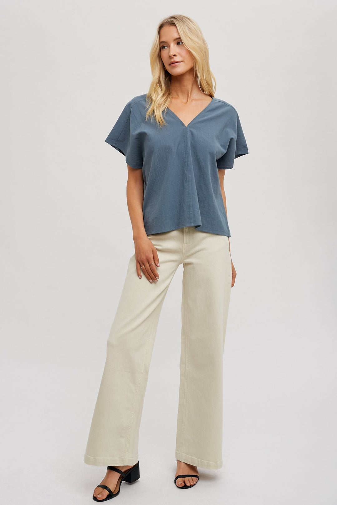 woman wearing a beige FUN2FUN V-neck top with dolman sleeves, showcasing an outfit with white bottoms.