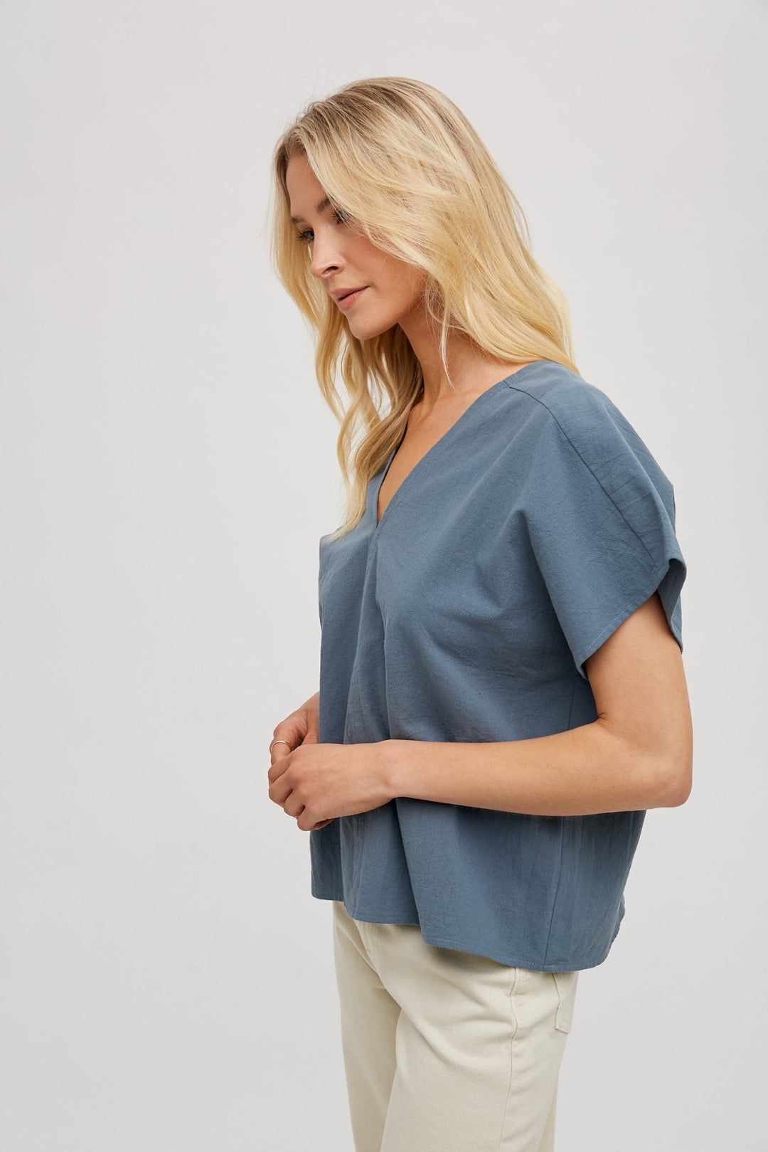 woman wearing a beige FUN2FUN V-neck top with dolman sleeves, showcasing the side view.