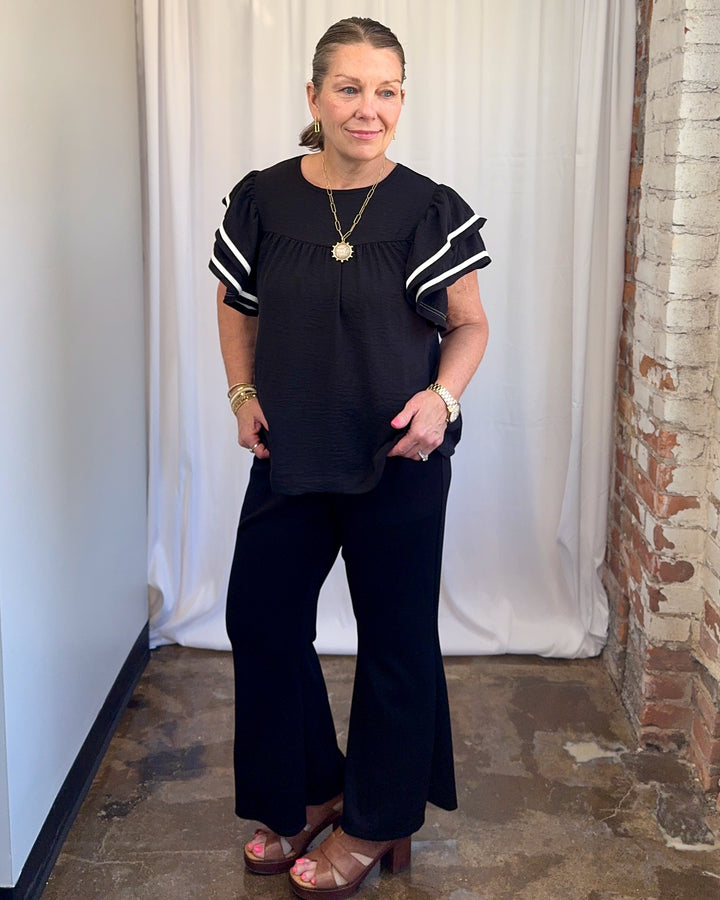 Carole Christian Game Day Ruffle Sleeve Textured Top in Black — full front outfit view styled with black wide-leg trousers and brown platform sandals, model wearing Small, Modish Maven Boutique