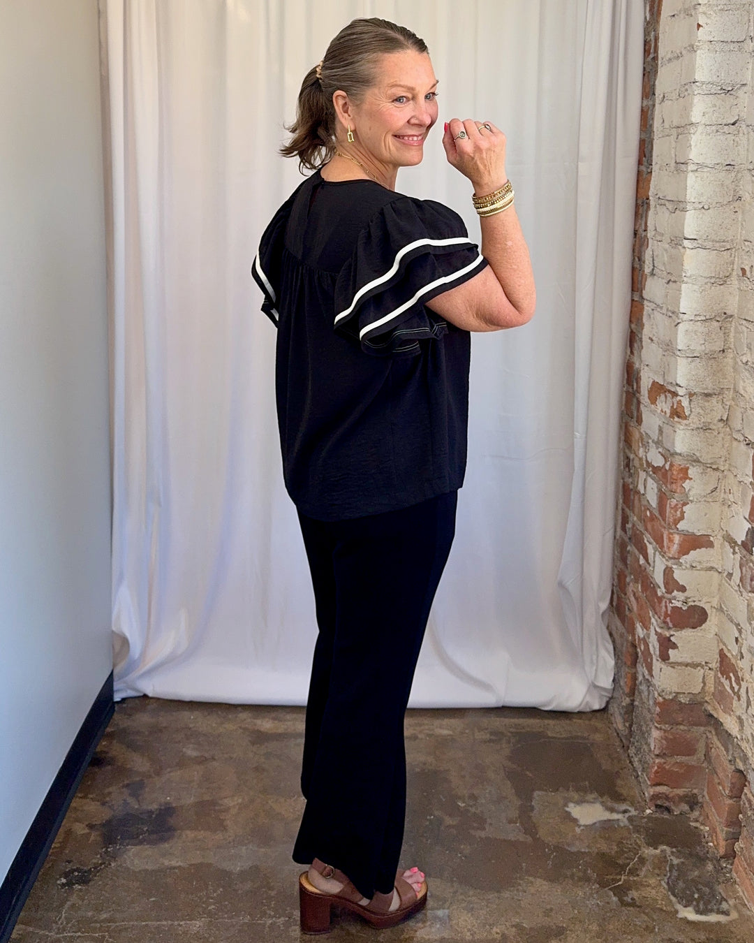 Carole Christian Game Day Ruffle Sleeve Textured Top in Black — side-back full length view styled with black wide-leg trousers and brown platform sandals, model wearing Small, Modish Maven Boutique