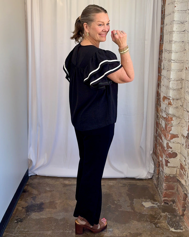 Carole Christian Game Day Ruffle Sleeve Textured Top in Black — side-back full length view styled with black wide-leg trousers and brown platform sandals, model wearing Small, Modish Maven Boutique