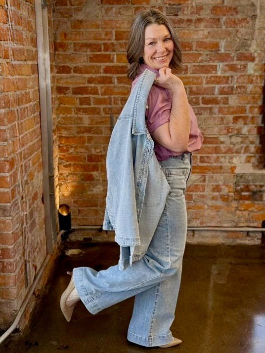 Dear John Denim Gina Relaxed Fit Denim Jacket in Zurie wash held over shoulder, styled with pink button-down and wide-leg jeans, side pose on model
