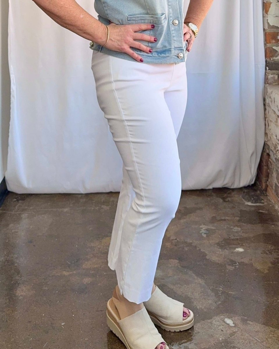 Person wearing white pants and a denim jacket in an indoor setting with a white curtain and brick wall.