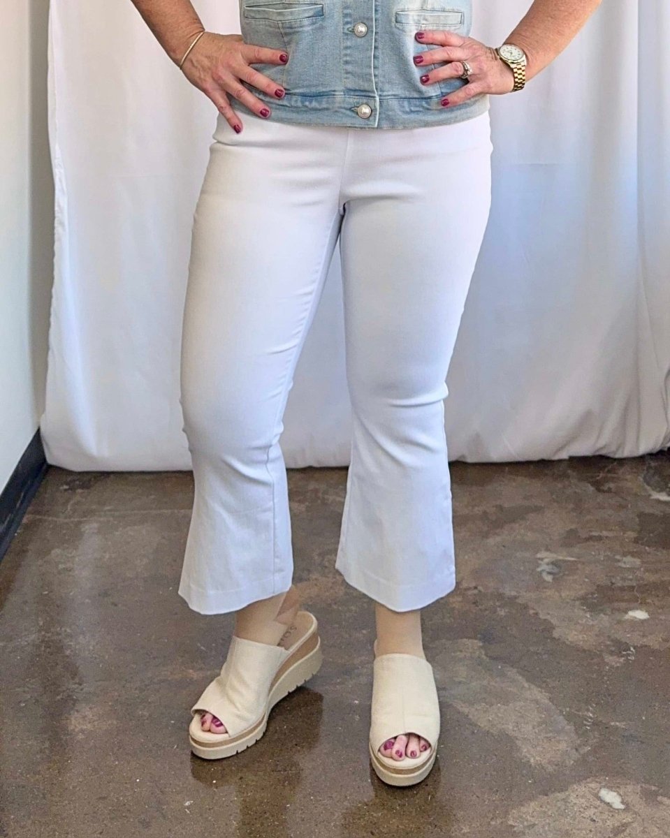 Person wearing white jeans and beige sandals against a plain background