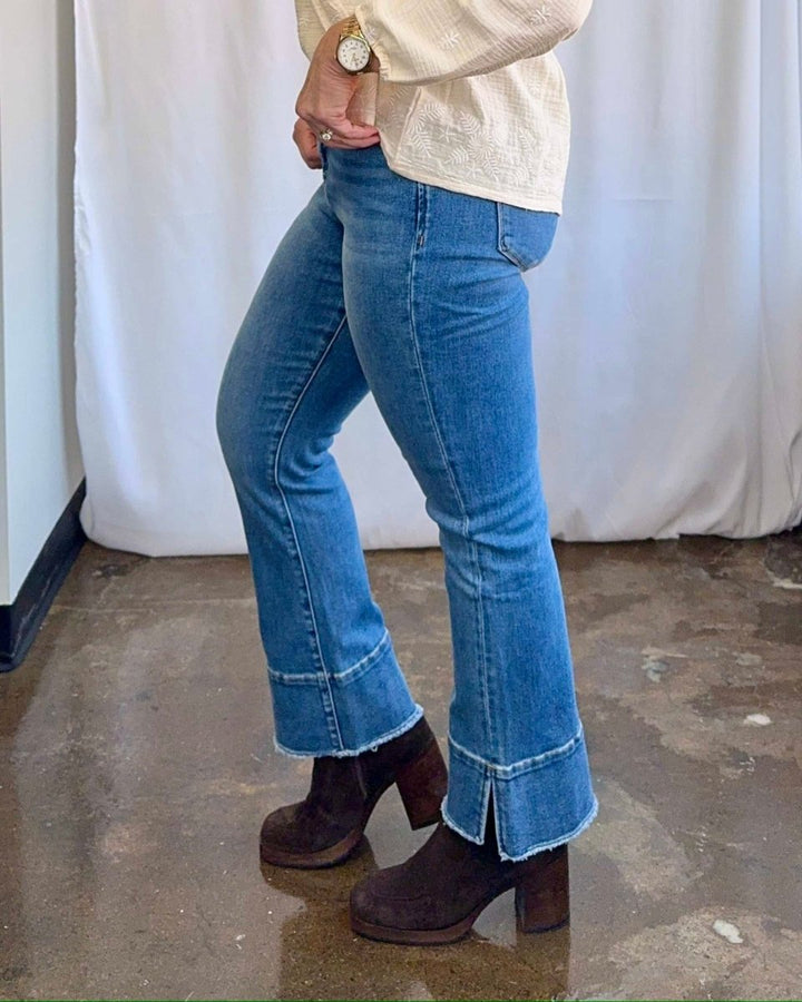 Person wearing blue flared jeans and brown clogs against a white curtain background