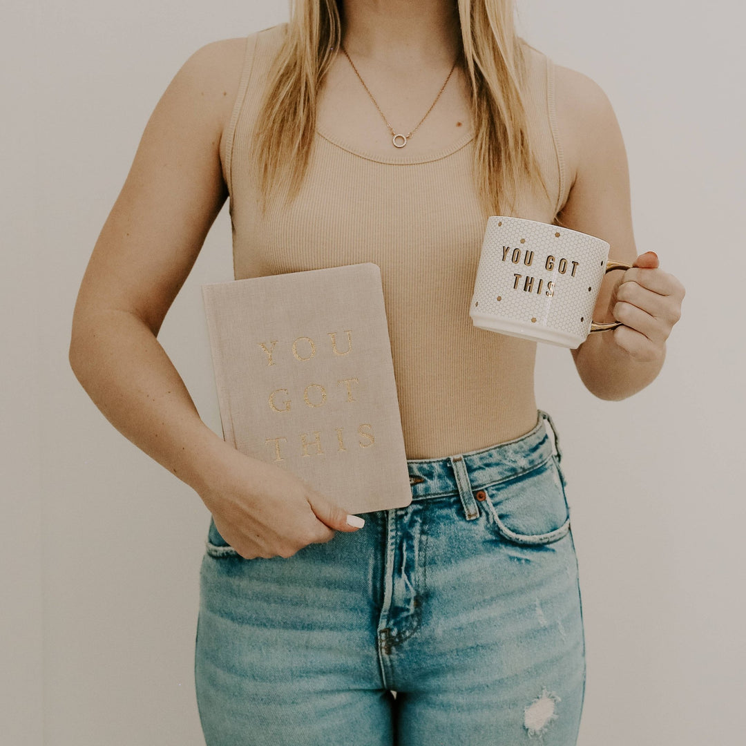 woman holding a journal and coffee mug.
