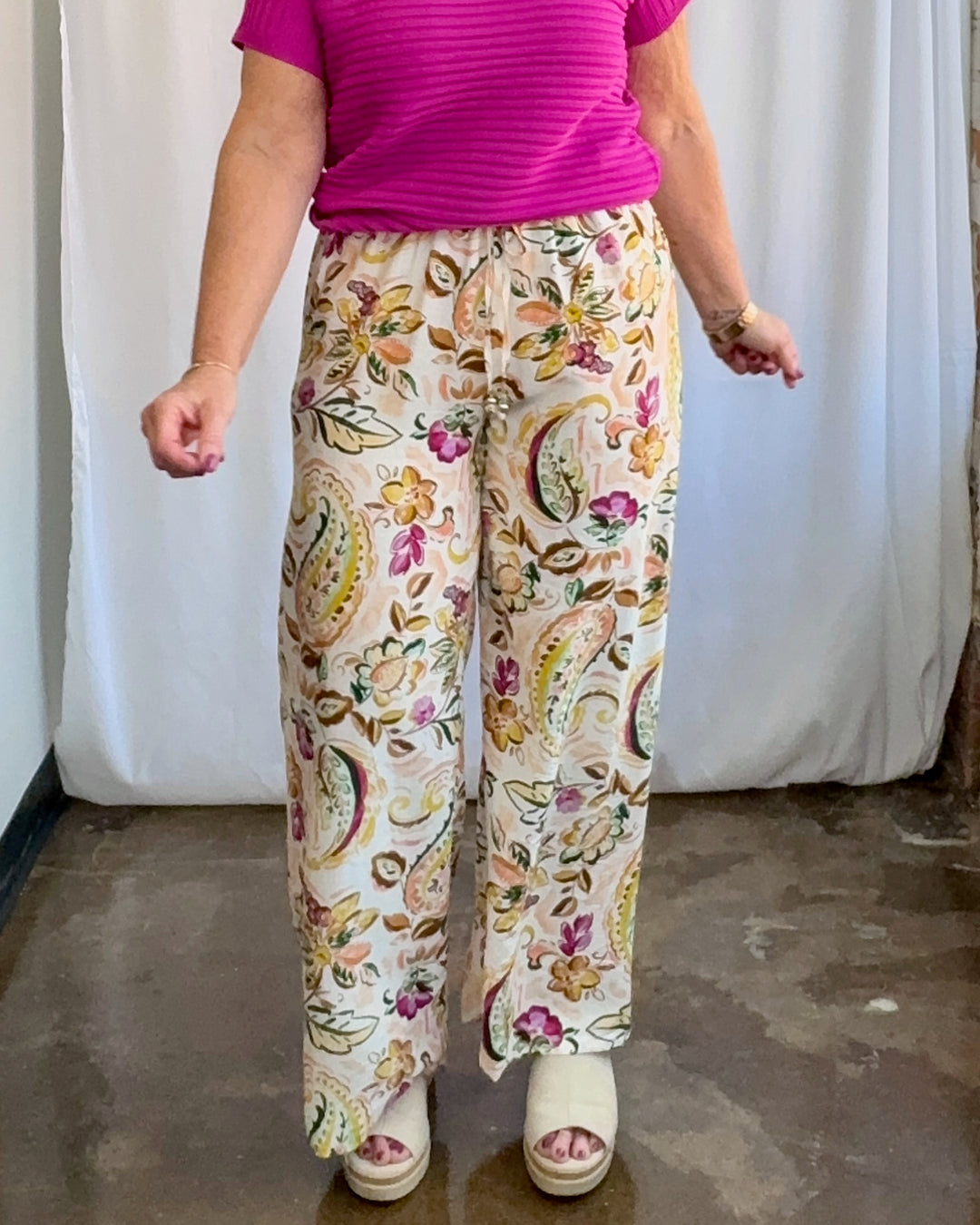 Person wearing a pink top and floral pants against a white curtain background