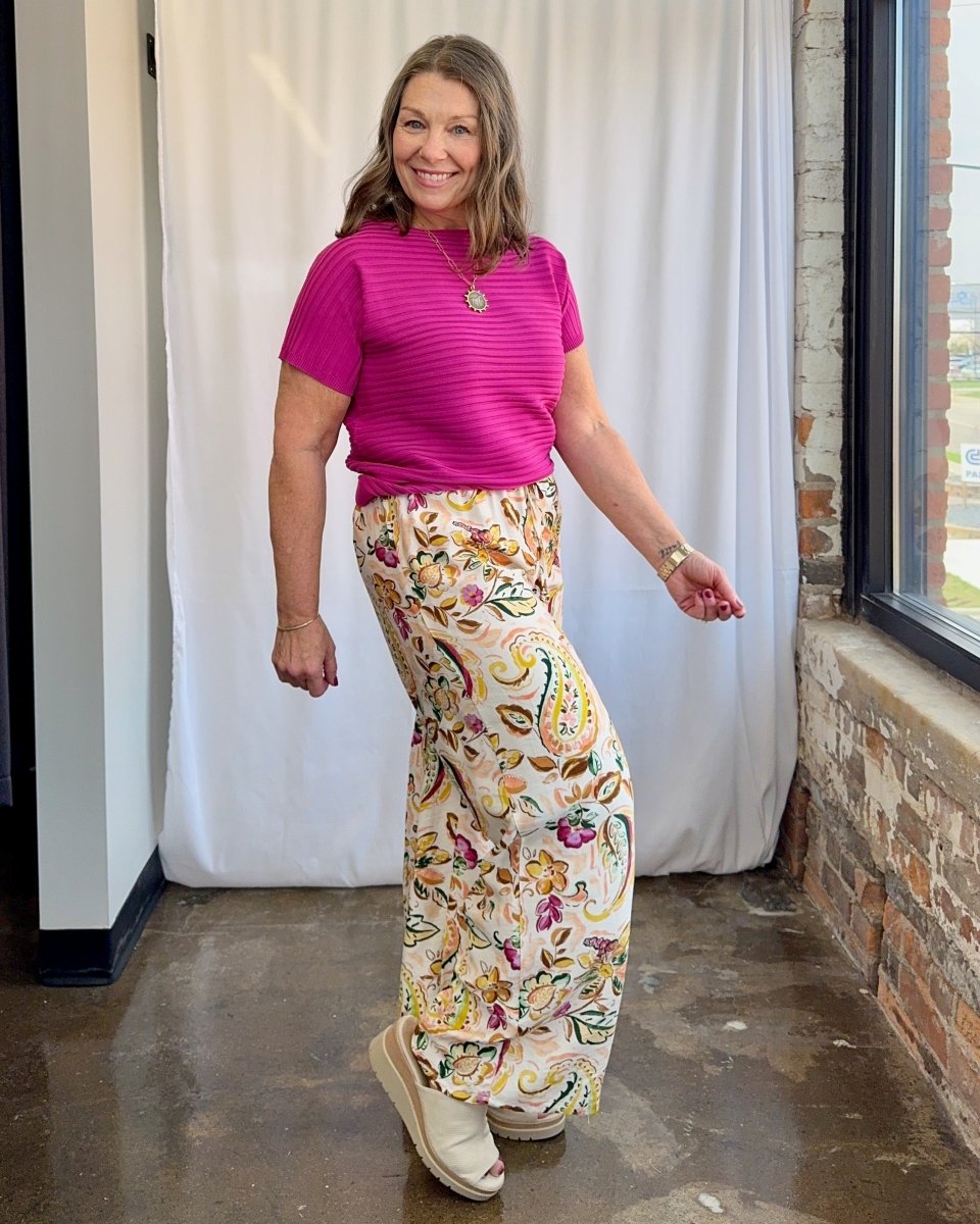 Woman wearing a pink top and floral pants standing indoors.