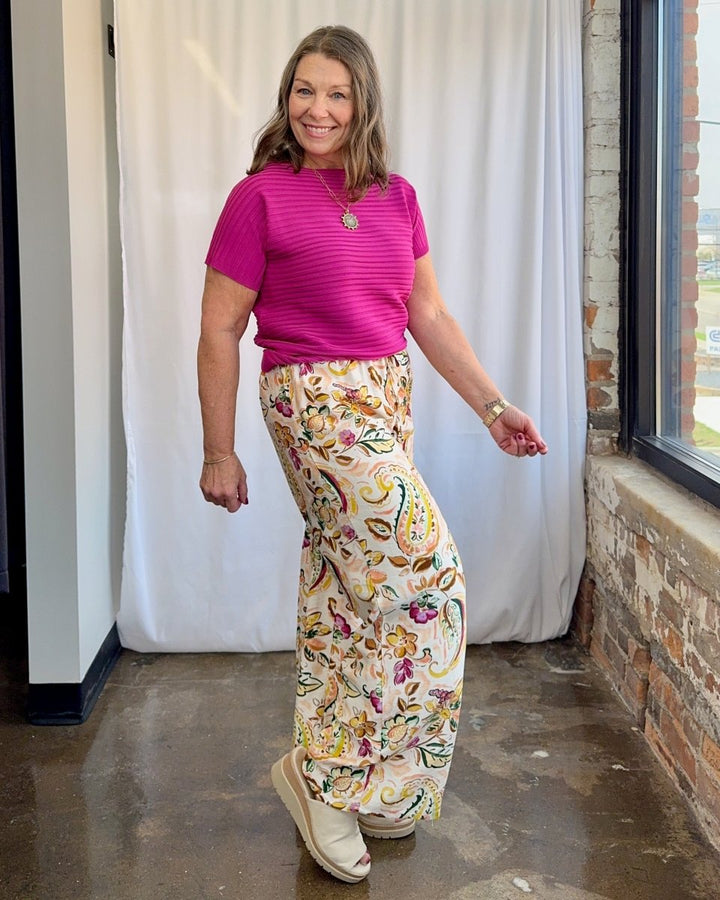 Woman wearing a pink top and floral pants standing indoors.