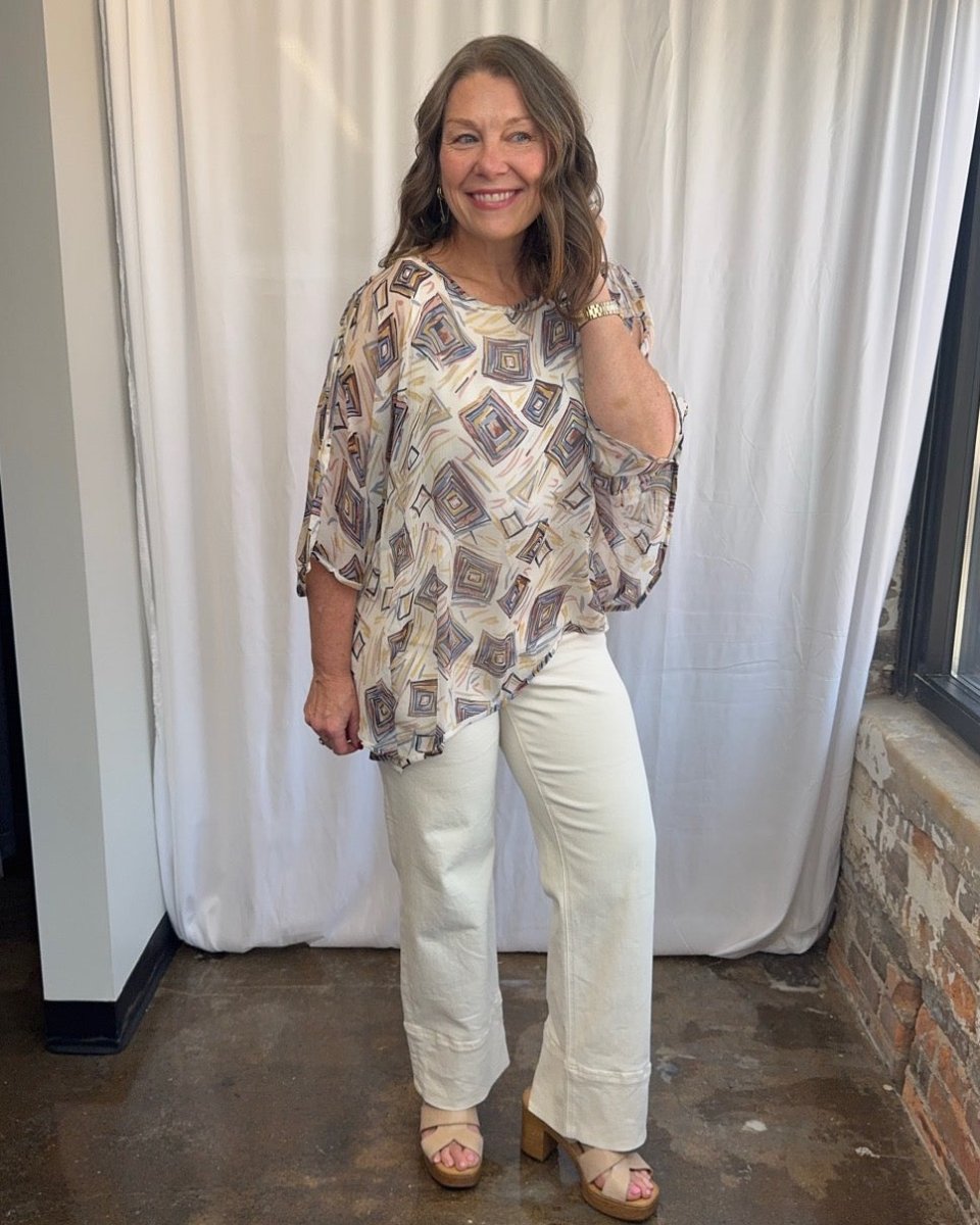 Lior Geometric Diamond Print Asymmetrical Blouse in cream styled with white wide-leg denim and wood block heel sandals, smiling full length front view on model
