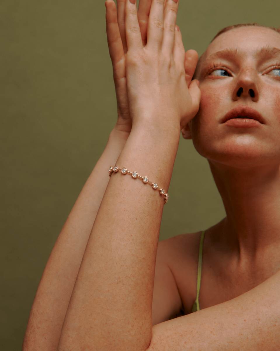 Lora Bezel Bracelet in Gold — worn on raised wrist against an olive background