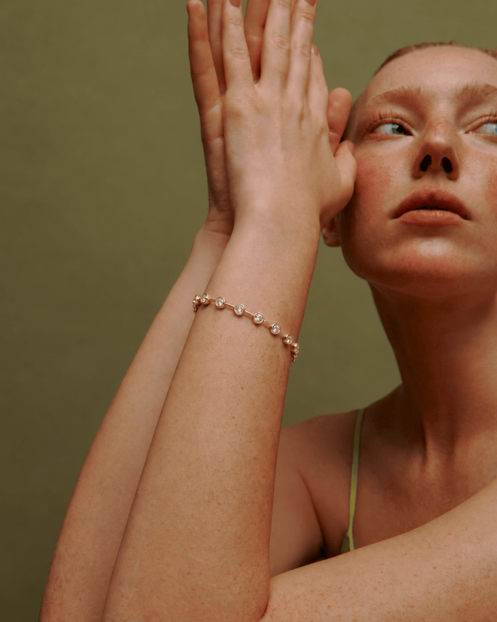 Lora Bezel Bracelet in Gold — worn on raised wrist against an olive background