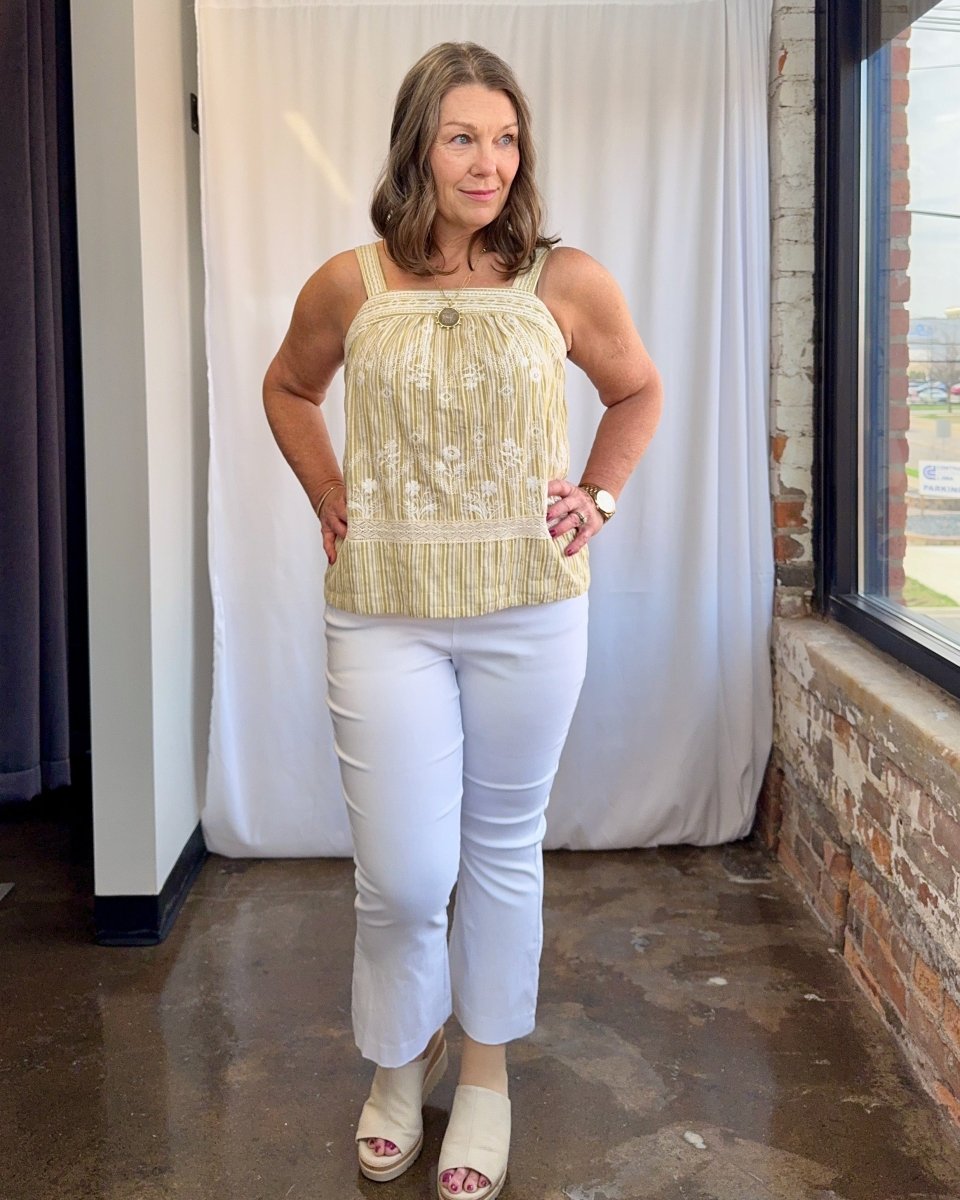 Woman wearing a light-colored top and white pants standing indoors.