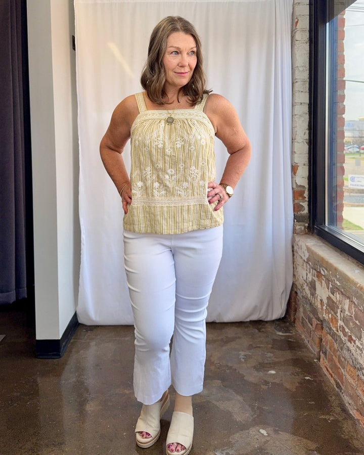 Woman wearing a light-colored top and white pants standing indoors.