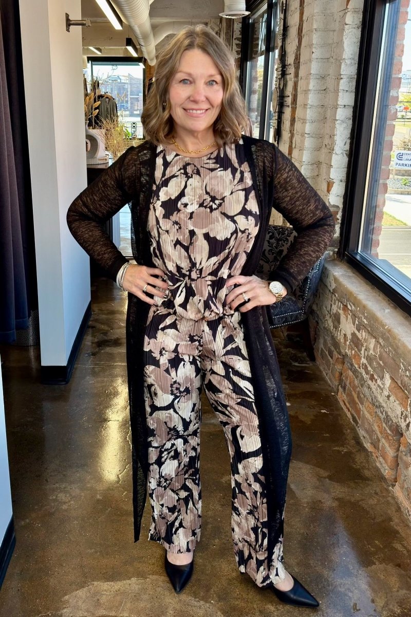 A woman modeling a sophisticated floral print jumpsuit paired with a long, sheer black open-front cardigan for a layered, effortless look.