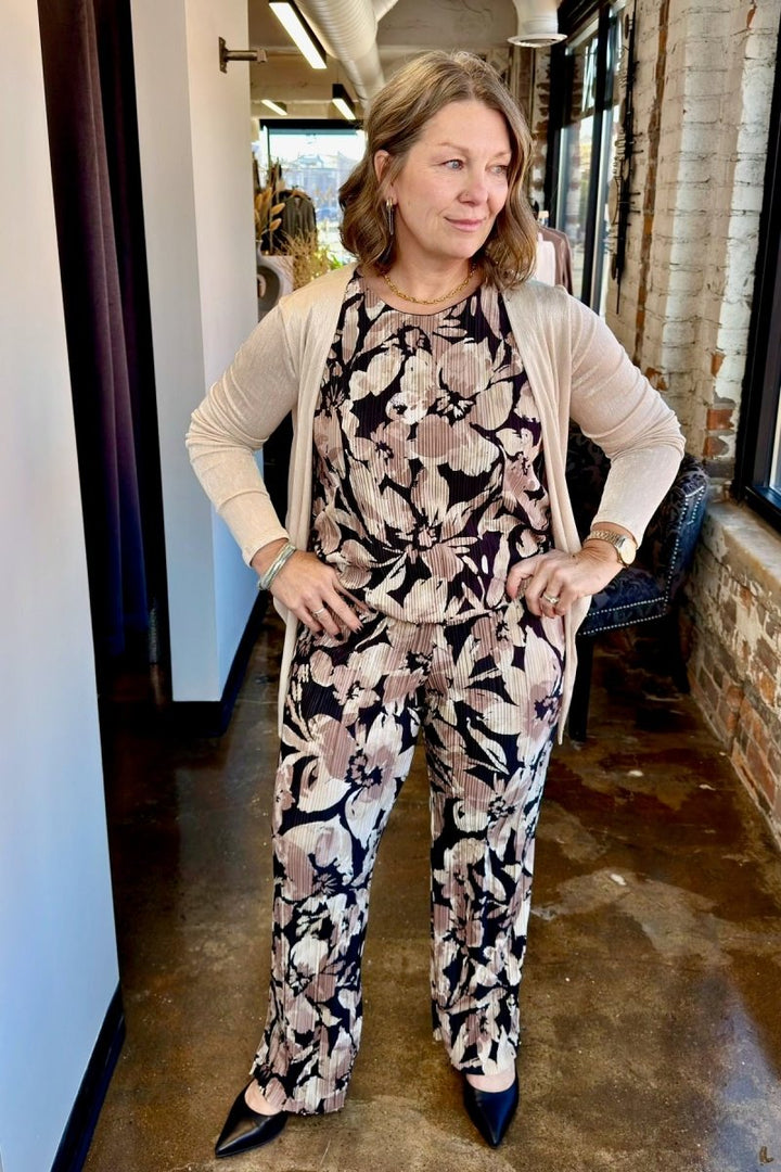 A chic outfit featuring a sleeveless floral jumpsuit layered under a lightweight cream-colored cardigan, showcasing an elegant and airy style perfect for transitioning seasons.