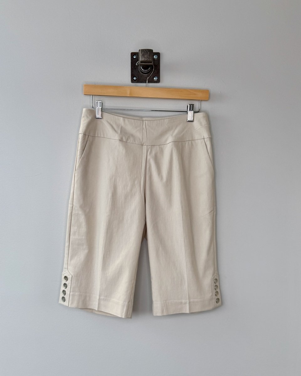 Beige shorts hanging on a wooden hanger against a gray wall.