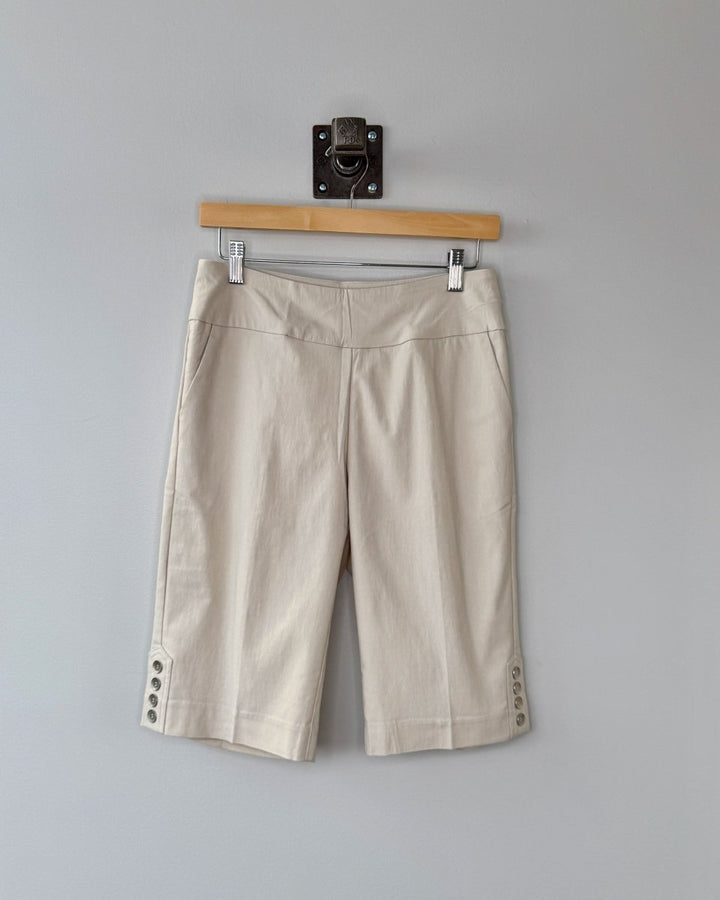 Beige shorts hanging on a wooden hanger against a gray wall.