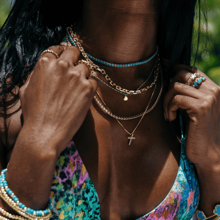 Raya CZ Cross in Gold — close-up of cross below layered chains and turquoise accents