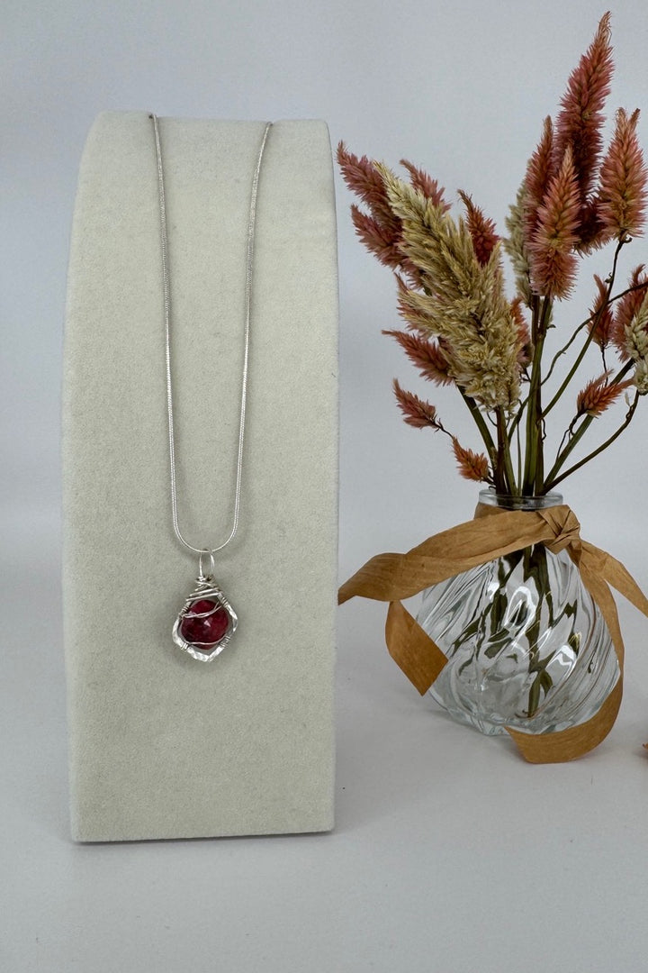 Raw Ruby Wire-Wrapped Pendant Necklace in Red &amp; Silver — necklace displayed next to dried flowers