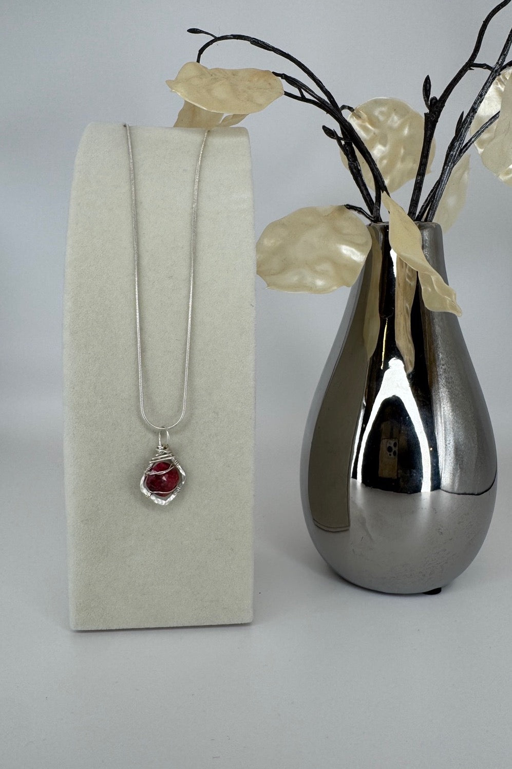 Raw Ruby Wire-Wrapped Pendant Necklace in Red & Silver — pendant displayed beside a decorative vase