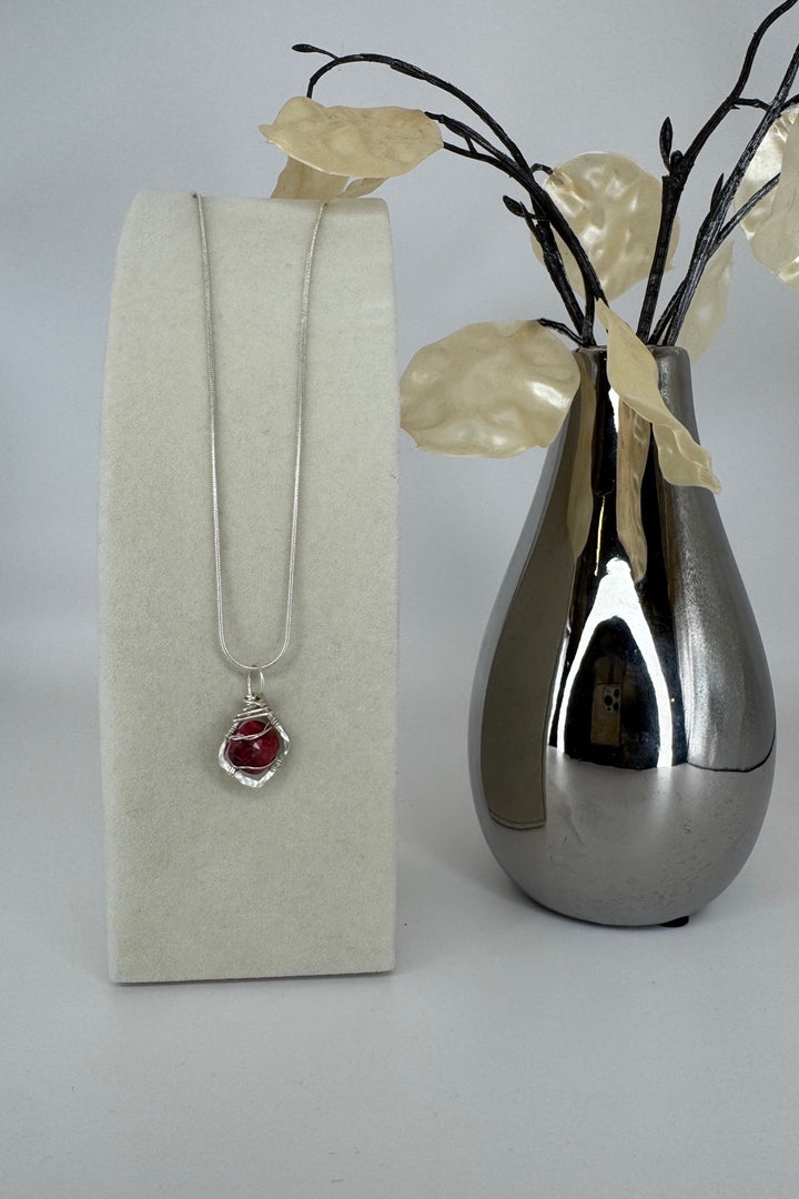 Raw Ruby Wire-Wrapped Pendant Necklace in Red &amp; Silver — pendant displayed beside a decorative vase