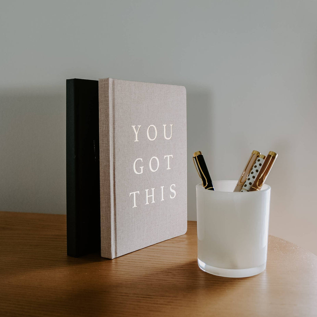 two journals standing on end with a cup of pens next to them.