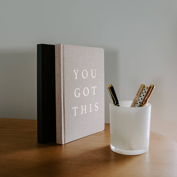 two journals standing on end with a cup of pens next to them.