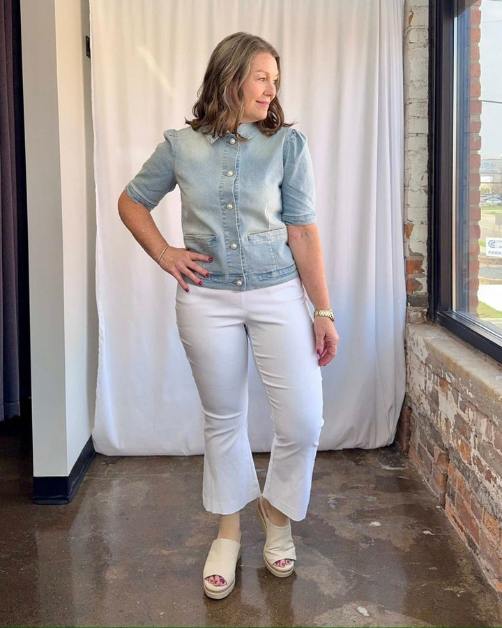 Woman wearing a denim jacket and white pants standing indoors.