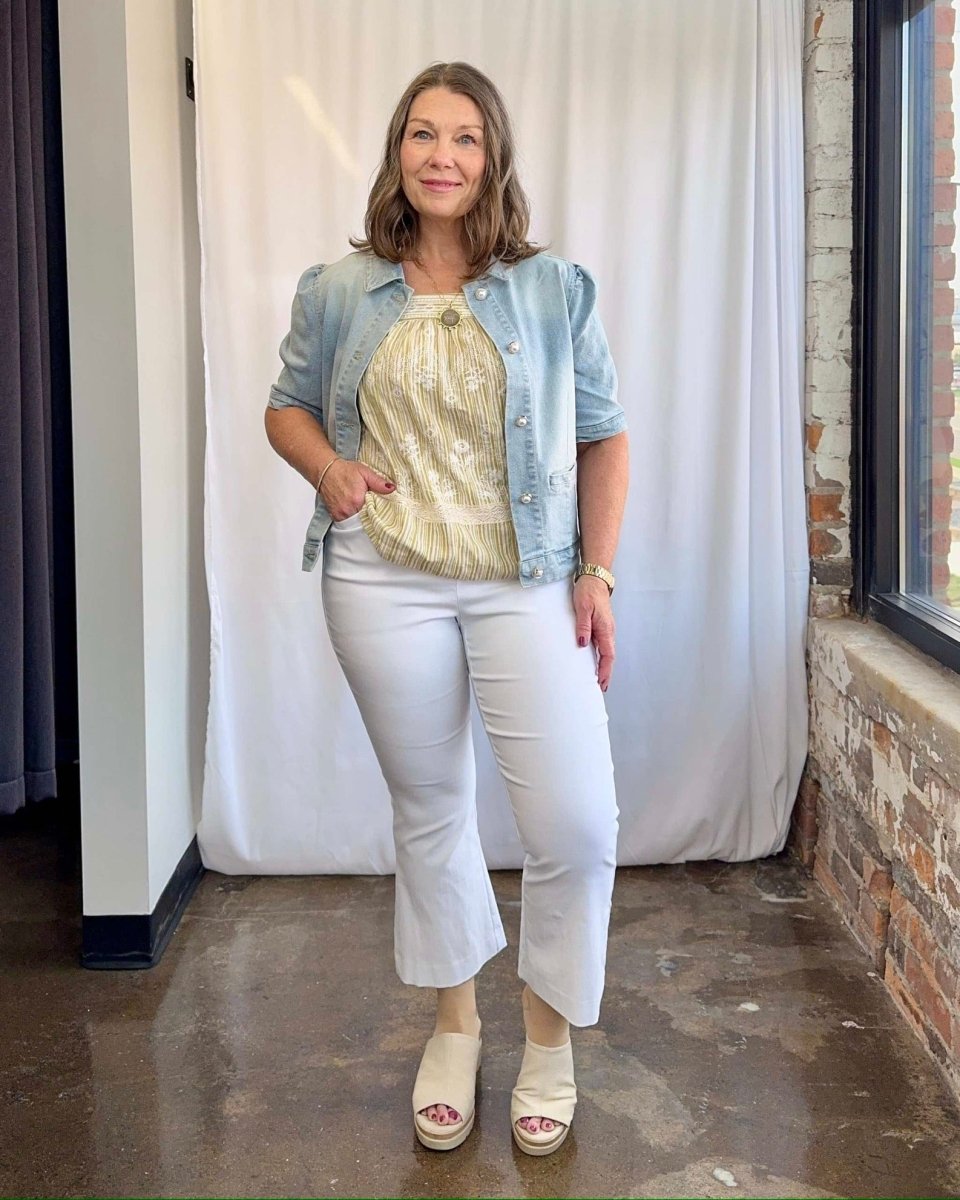 Woman wearing a denim jacket, gold top, and white pants in an indoor setting.