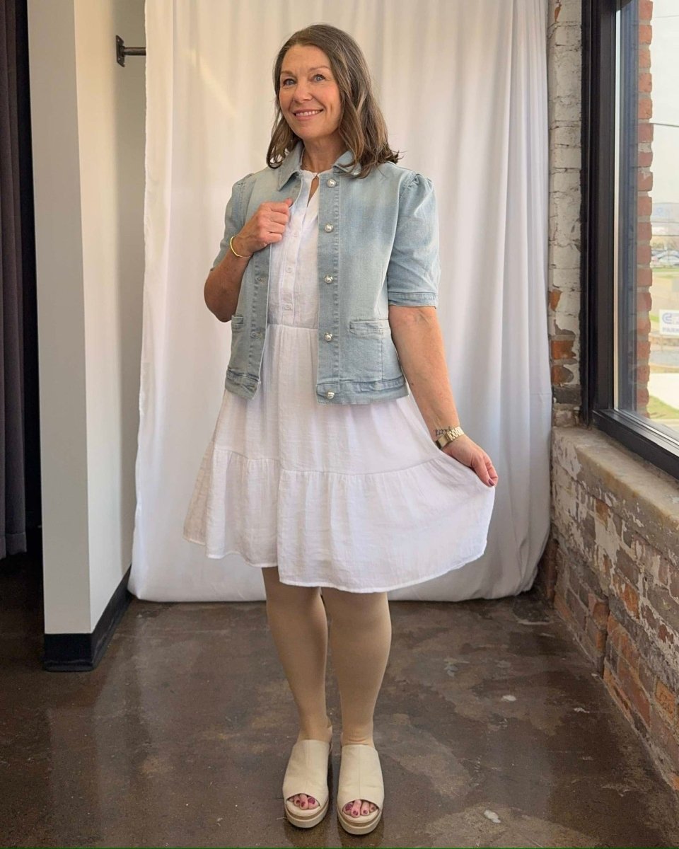 Woman wearing a white dress with a denim jacket in an indoor setting.