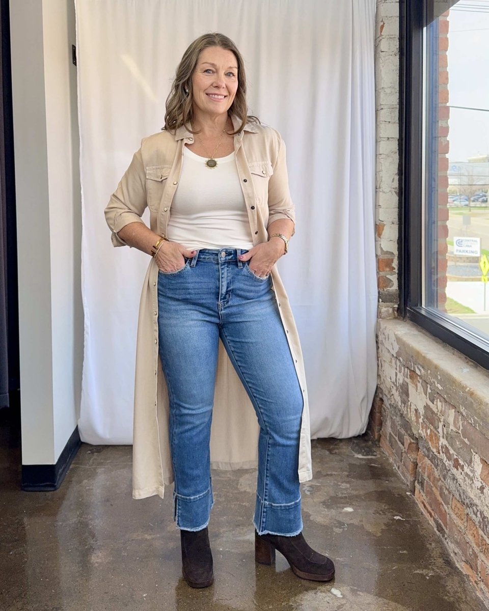 Woman wearing a beige cardigan, white shirt, blue jeans, and brown boots indoors.