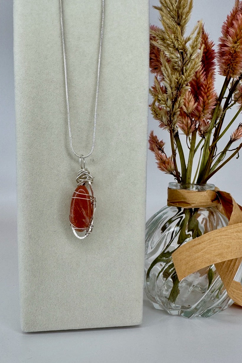 Wire-Wrapped Sunstone Pendant Necklace in Orange & Silver — pendant hanging beside dried flowers