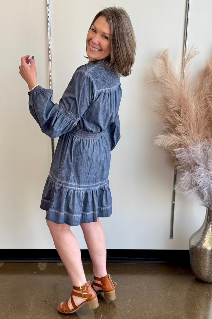 Smiling woman looking over her shoulder wearing a dark blue flowy, cinched waist dress.