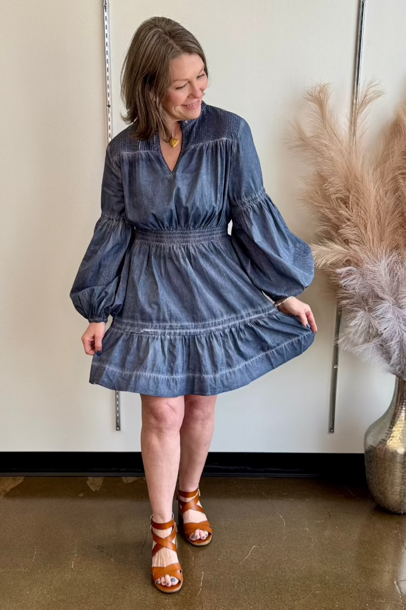 Woman looking down smiling and holding her blue dress out to show the ruffle detail of the skirt.