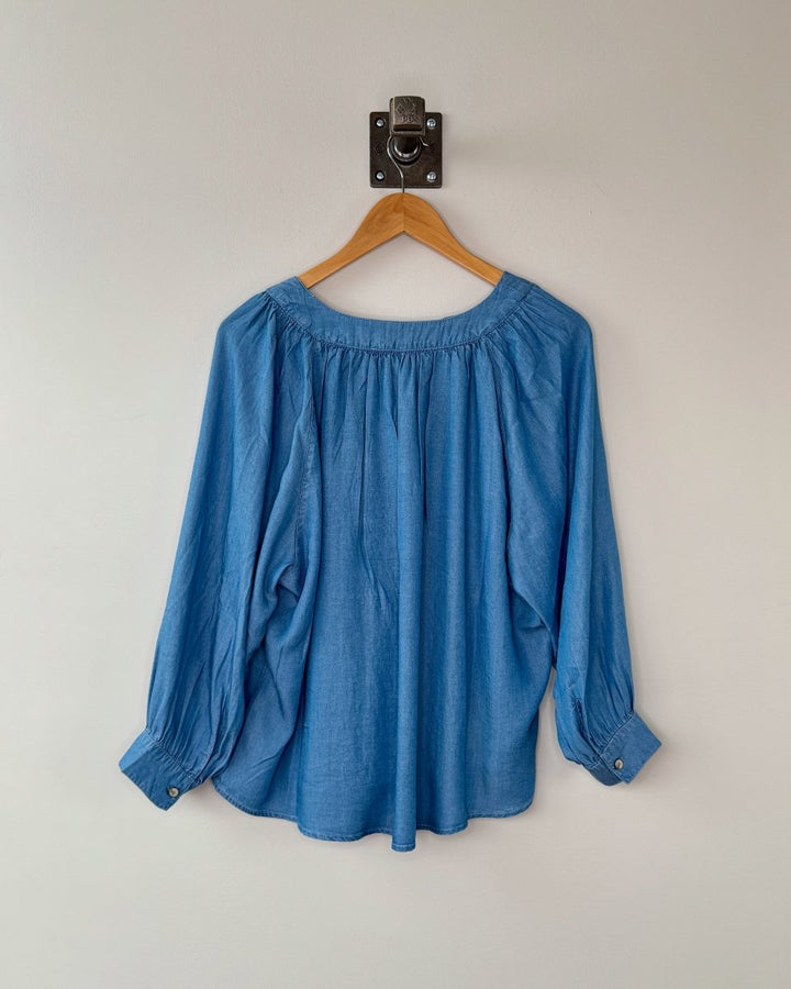 Blue blouse on a wooden hanger against a plain background