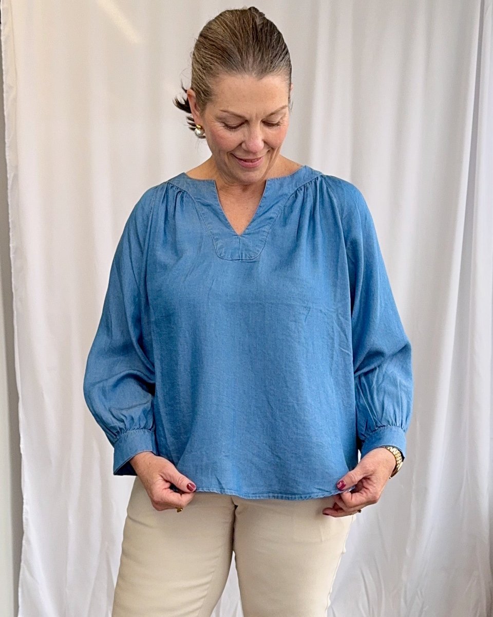 Woman wearing a blue blouse against a white curtain background