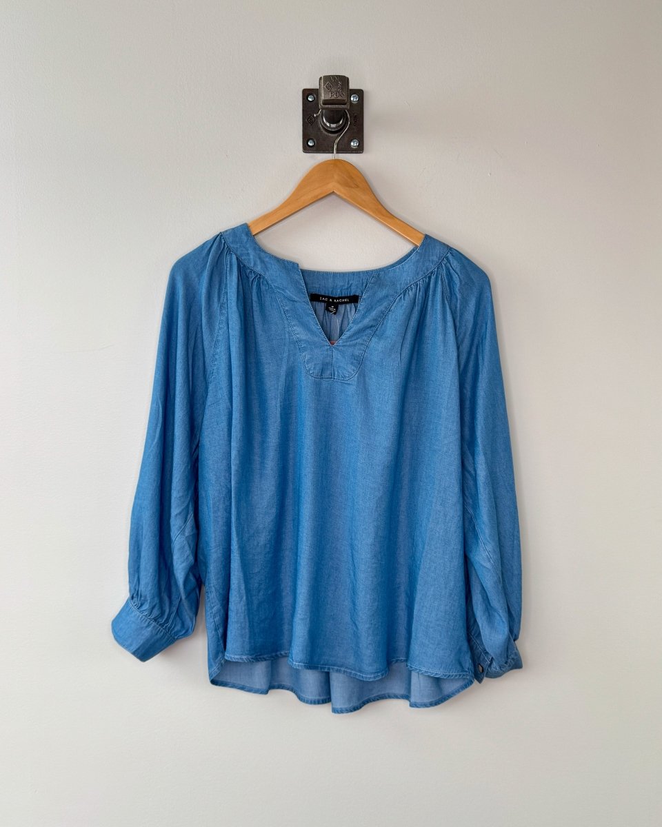 Blue blouse on a wooden hanger against a white wall