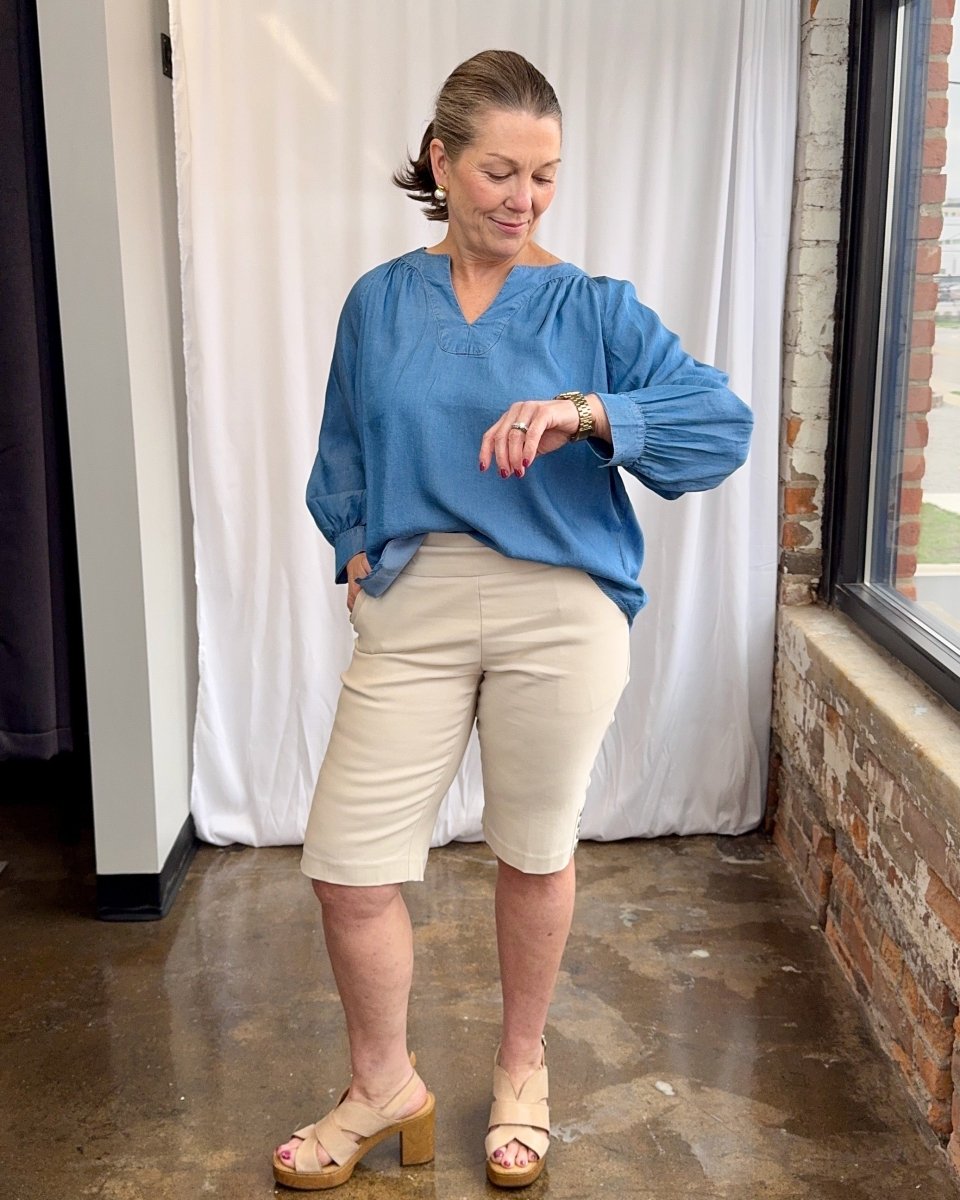 Woman wearing a blue blouse and beige shorts standing indoors.