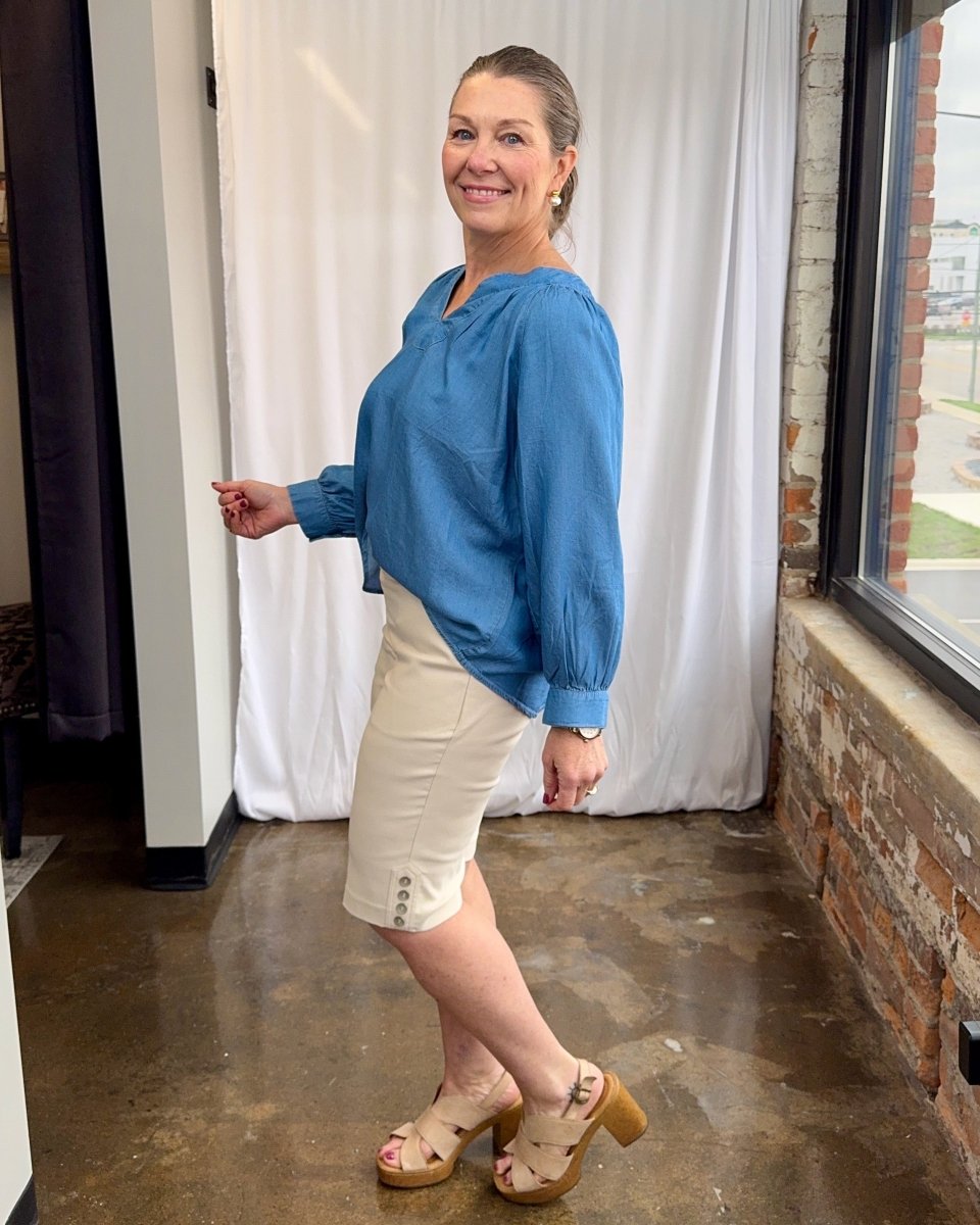 Woman wearing a blue blouse and white shorts standing indoors.