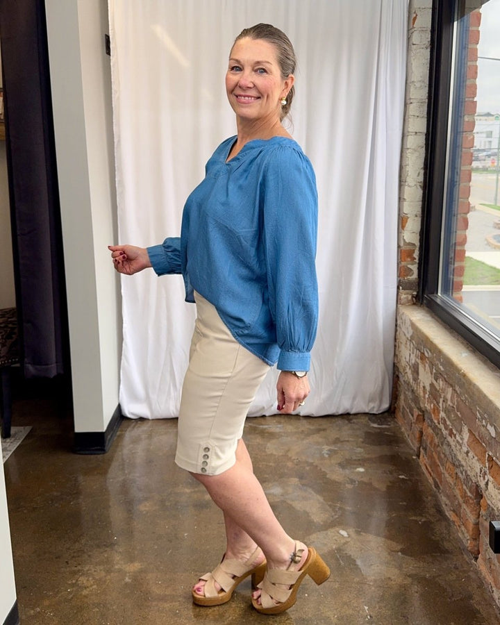 Woman wearing a blue blouse and white shorts standing indoors.