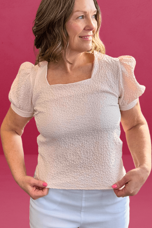 Woman wearing a cream textured top with a square neckline and feminine princess sleeves.