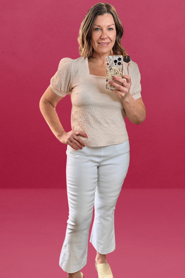 Woman wearing a light pink textured top with a square neckline and feminine princess sleeves.