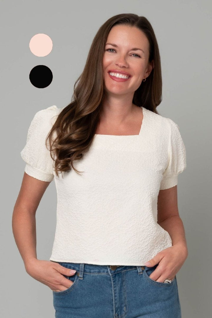 Woman wearing a cream textured top with a square neckline and feminine princess sleeves.