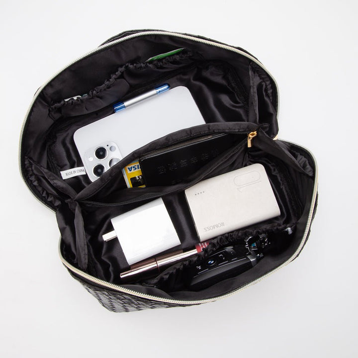 Open black makeup bag with cosmetic items including a phone, power bank, and brushes on a white background