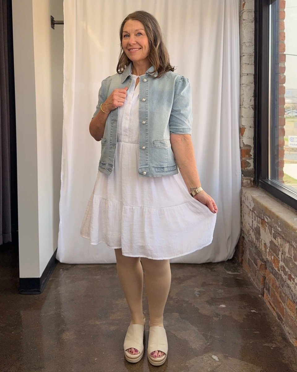 Woman wearing a white dress with a denim jacket in an indoor setting.