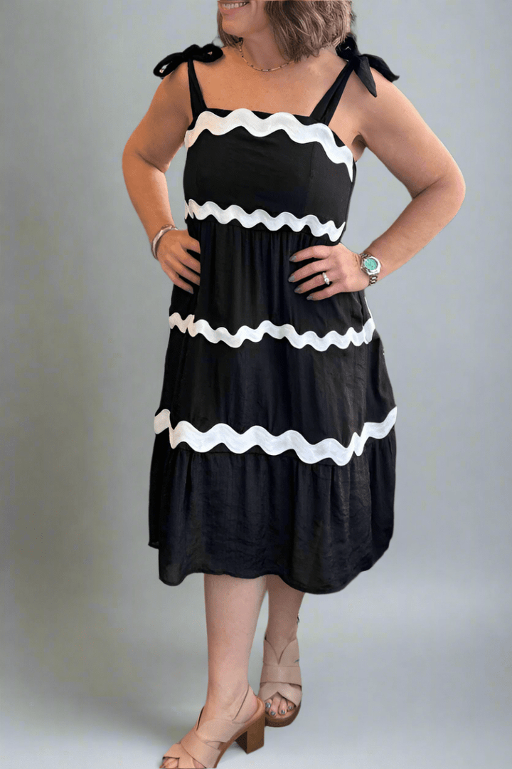 Front view of the Tissue Faille Ric Rac Dress in black with white wavy trim and adjustable shoulder ties.