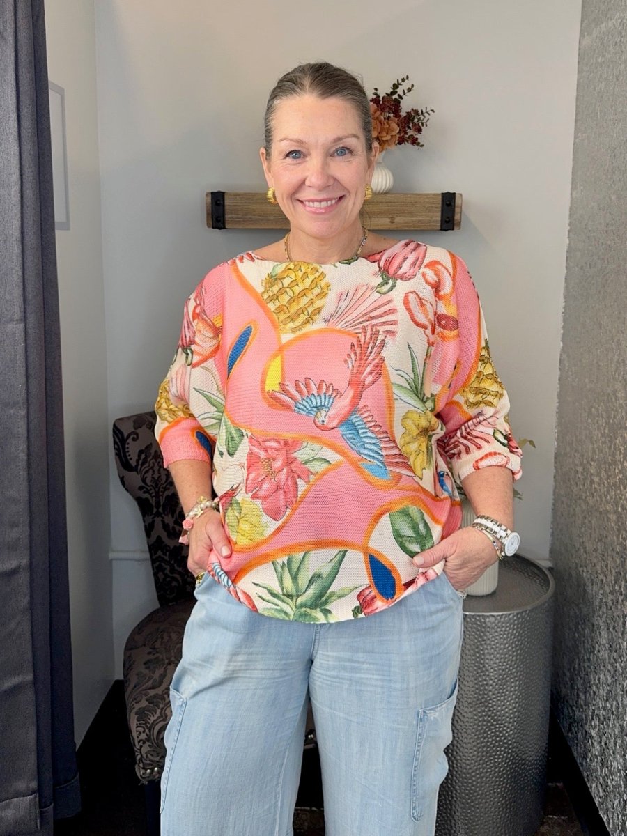 Smiling woman wearing a Coral Multi tropical print batwing sweater with 3/4 sleeves and light wash denim jeans.